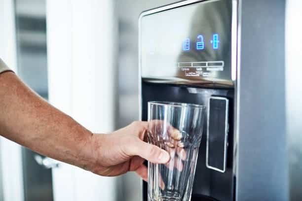 Unrecognizable man filling glass from refrigerator water dispenser