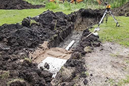 Installing a new mound septic system.  A spetic drainage pipe and electrical wire below a layer of sand and styrofoam insulation  in a freshly dug trench leading to where the septic tank will be installed.
