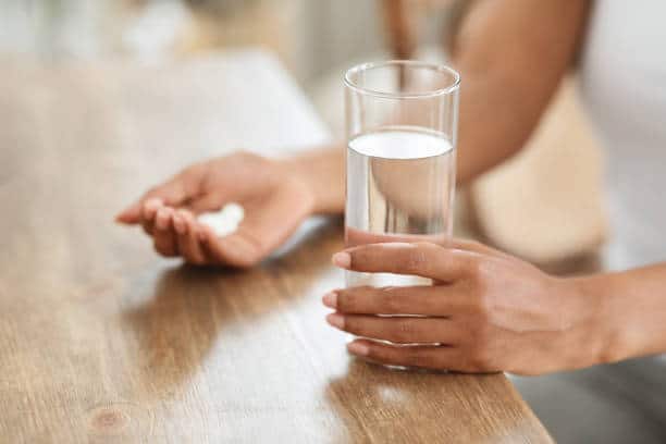 Unrecognizable black woman takes medicines with glass of water at home, cropped image, closeup