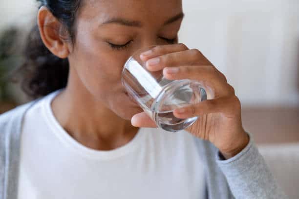 Close up african american young woman drinking clear water from glass cup. Concept of healthcare and good nutrition, water balance in body, wellness and good health, thirst and dehydration