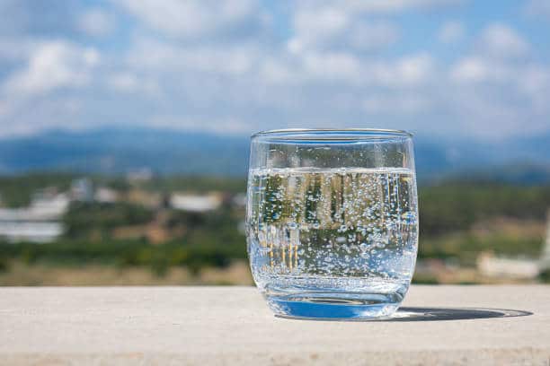 Sparkling water glass on a stone parapet with a mountain view. Cool glass of mineral water. Mountain mineral water
