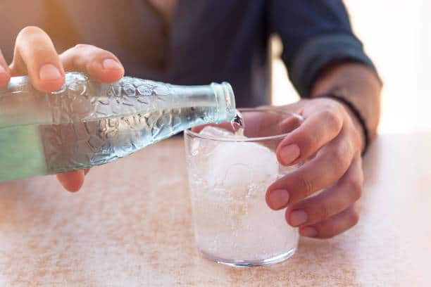 close-up adult man's hand pouring sparkling water into a glass of water outdoors
