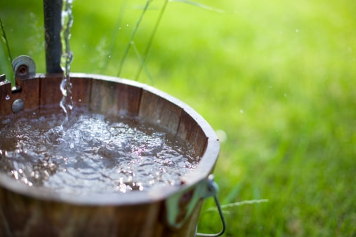 Fresh water from a well flows out into an old bucket. Shallow depth of field for focus on water.