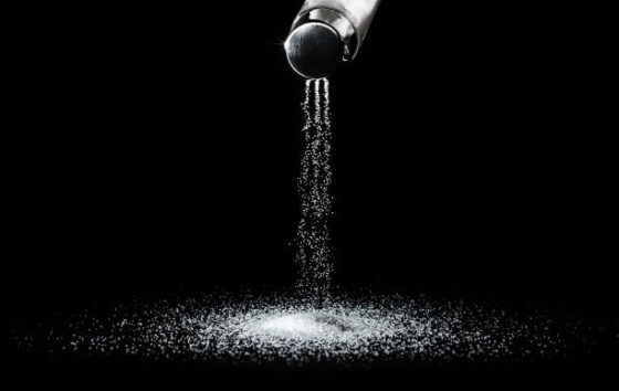 Salt spills out of the salt shaker in thin streams on a black background.Concept salting/
