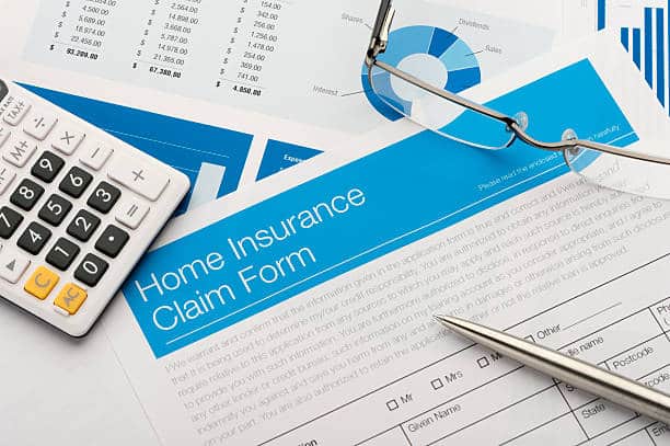 Home insurance claim form on a desk with paperwork. There is also a pen and calculator on the desk