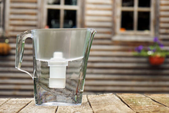Water filtration pitcher standing on a rough wooden table in front of the windows of a country house outdoors