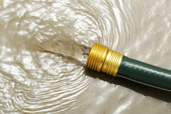 "Green gardening hose with running water on a concrete floor, wasting water."