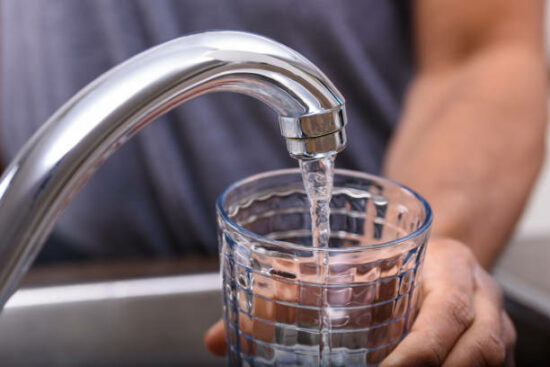 Hand with drinking glass filling water from kitchen faucet, home and lifestyle concept